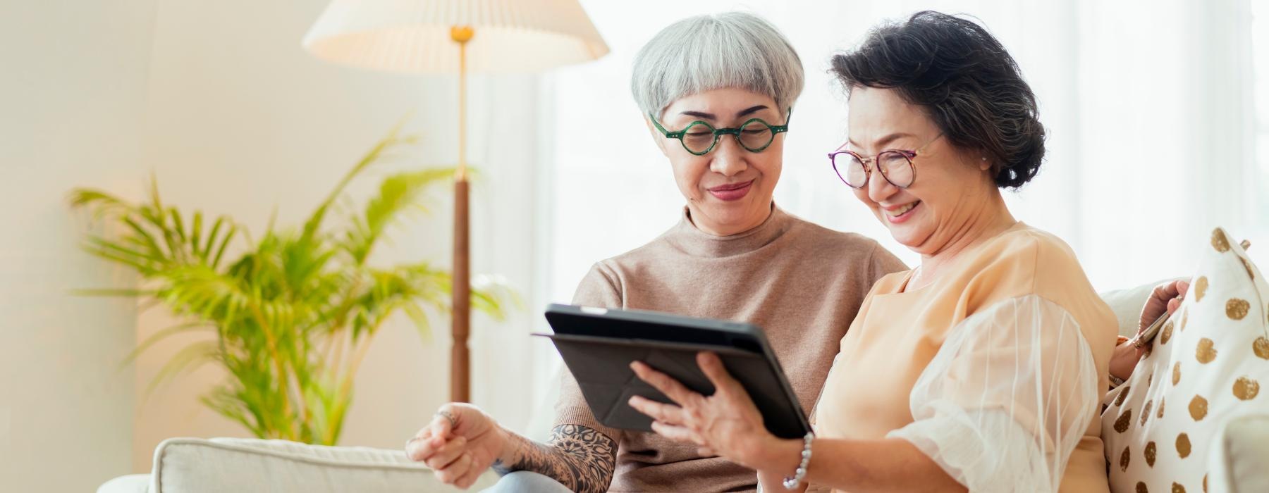 two woman sit on a couch looking at a tablet