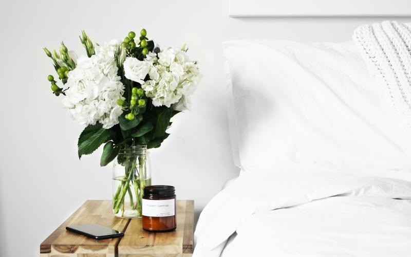 a vase of white flowers on a table next to a bed