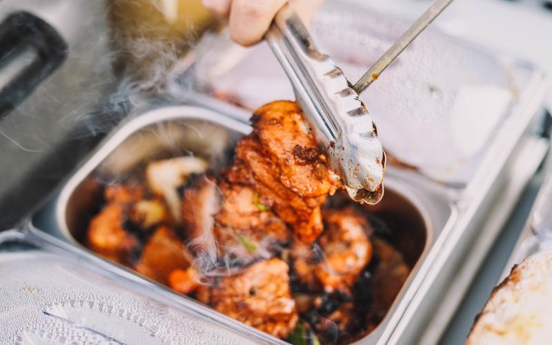 person picking up a skewer of meat with tongs